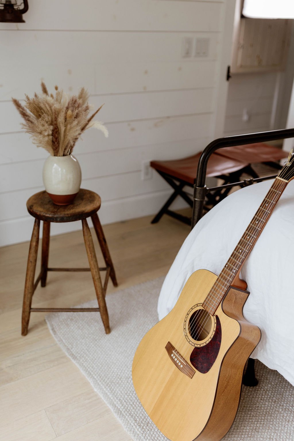 A handmade ceramic vase filled with dried grasses beside an acoustic guitar