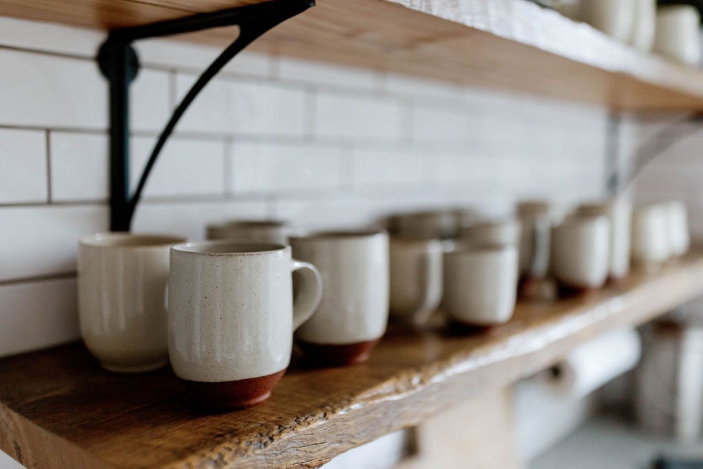 Handmade Ritual Ceramics mugs arranged on warm wooden shelves