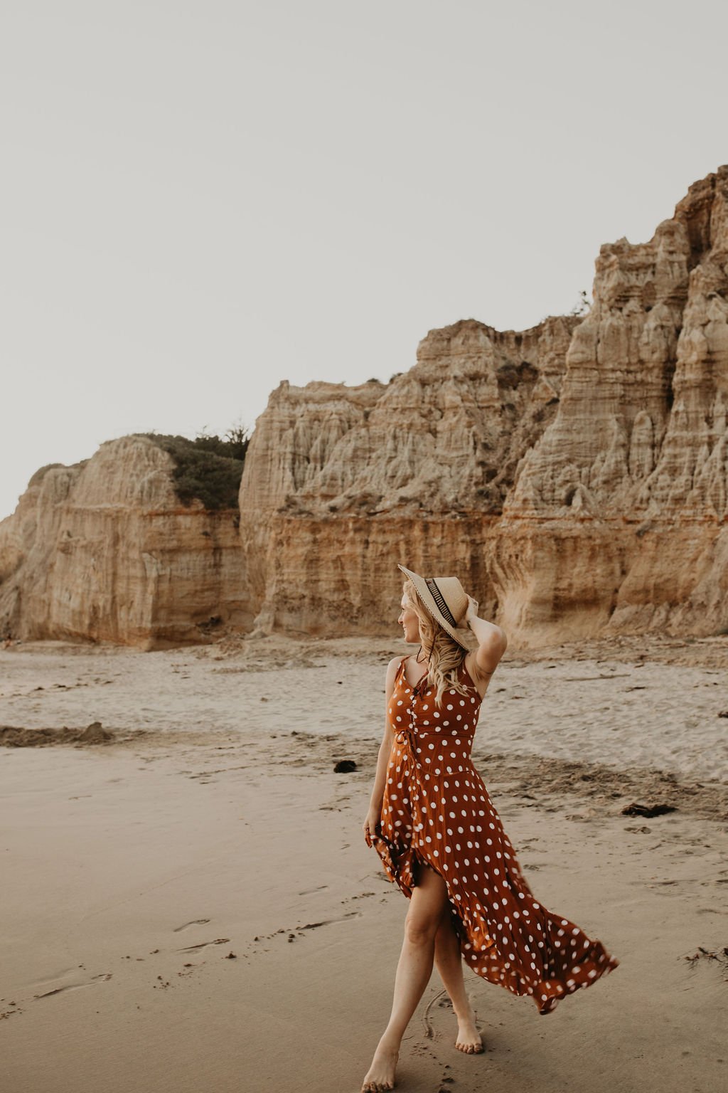 Kali May walking along the beach beneath warm coastal cliffs